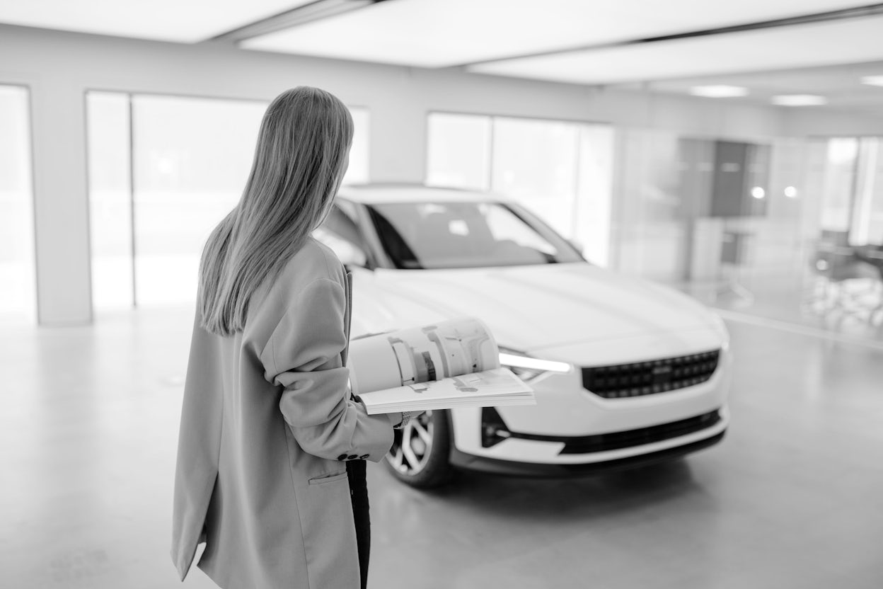 Black and white photo of Jenny Mustard standing in front of a white Polestar 2.