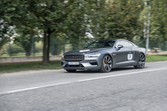 Polestar car driving on a road with trees and fencing in the background.