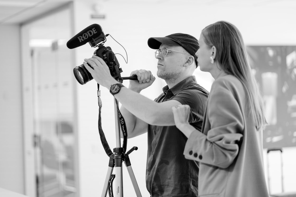 Black and white photo of Jenny Mustard and a photographer looking at a camera.