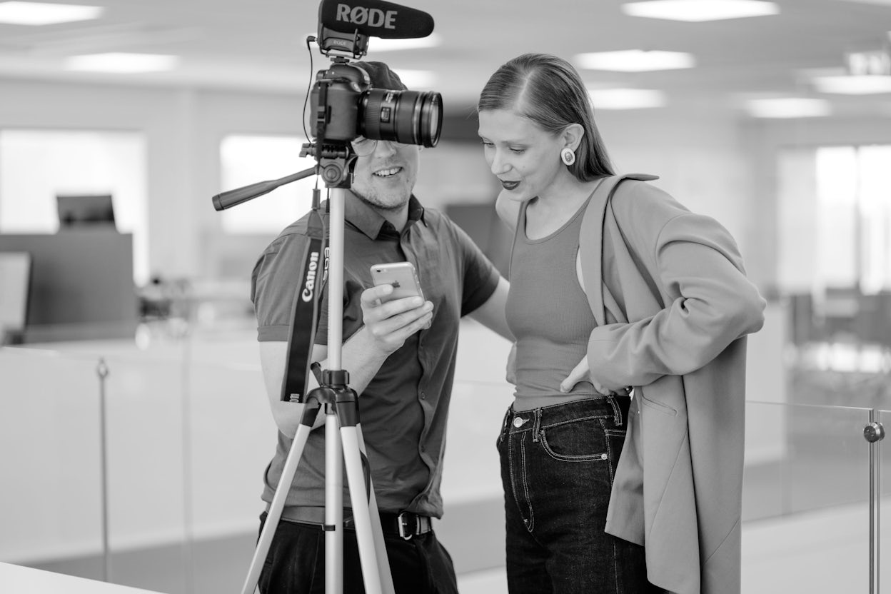 Black and white photo of Jenny Mustard and a photographer watching something together on a phone.