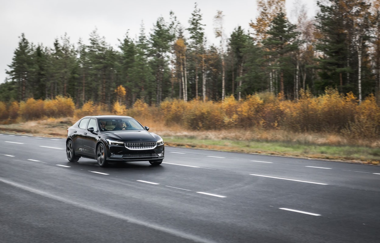 A black Polestar 2 driving on a forest road in autumn.