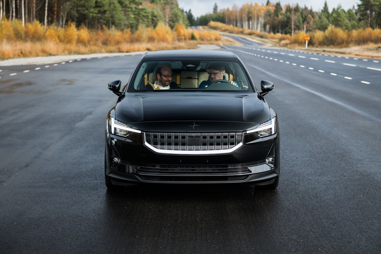 Two people sitting in the front seats of a black Polestar 2 on the road in autumn.
