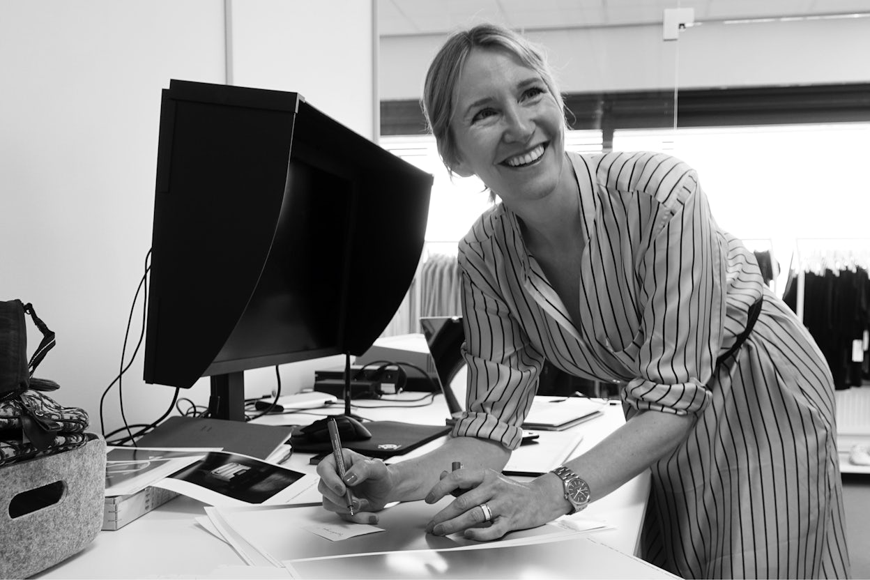 Smiling Susanne Blomster standing by her desk and holding a pen.