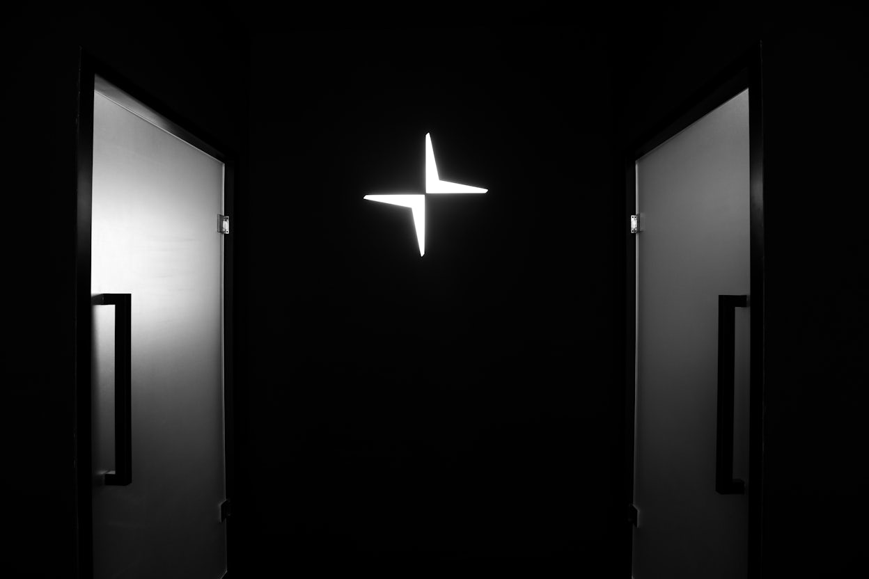 The Polestar logo in illuminated white on a black wall between two doors.