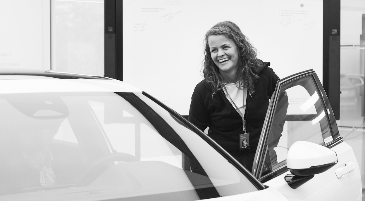 Smiling Polestar employee standing next to car with open front door.