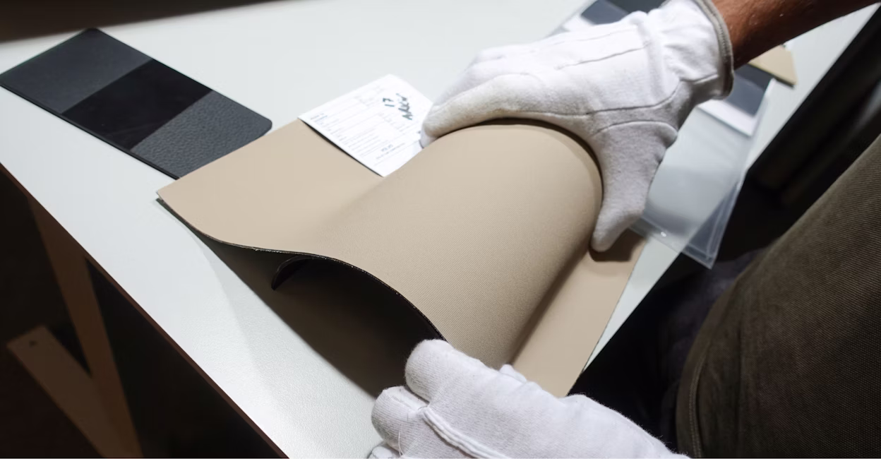 Two hands in white gloves holding a piece of leather.