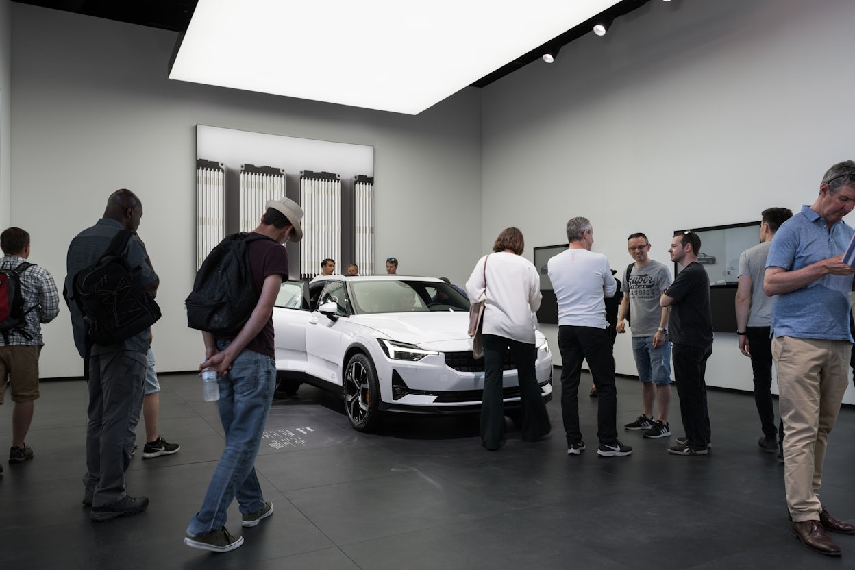 Crowd of spectators gathered around a white Polestar 2 in a minimalistic exhibition space.