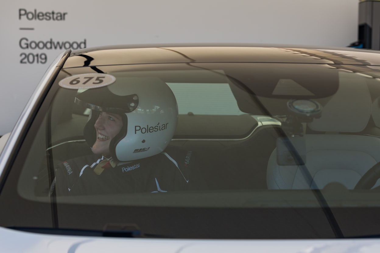Smiling woman, wearing a racing helmet, seated inside a Polestar 1 at the Goodwood Festival of Speed.