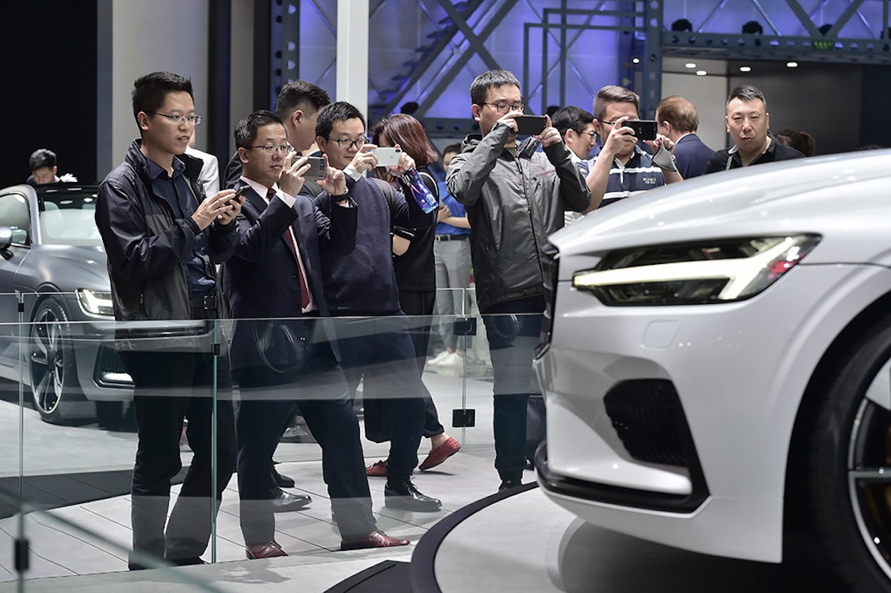 The front of a white Polestar 1 at a car event, with a group of enthusiastic men photographing it.