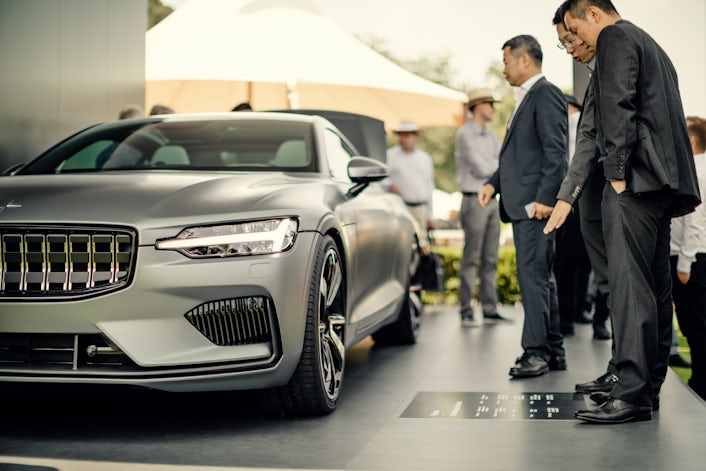 Two men reading a sign placed next to a metallic Polestar 1.