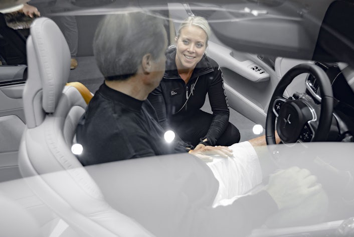 Man sitting behind the wheel of a Polestar talking to a woman kneeling next to the car.