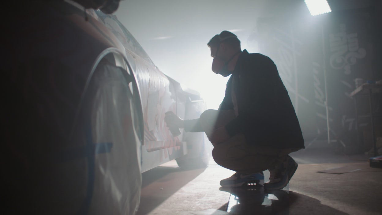 Tristan Eaton wearing a facemask while doing graffiti on a Polestar 1.