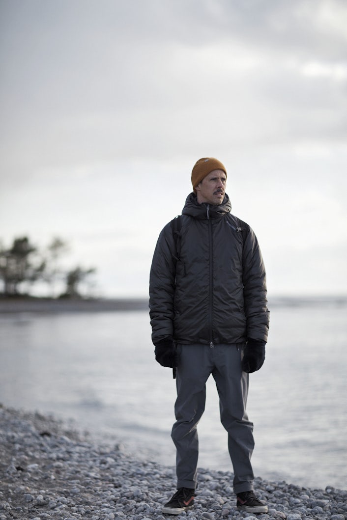 A person dressed in a black jacket and orange hat on a stone beach.