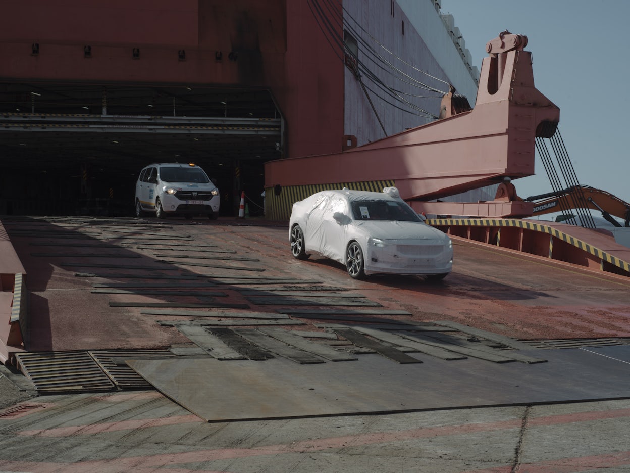 A Polestar 2 covered in protective plastic being driven down from a loading ramp.