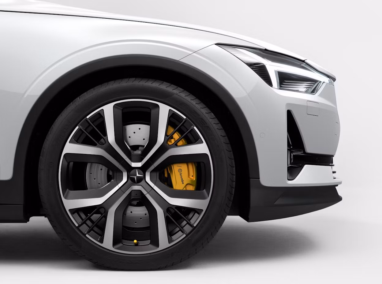 Front wheel and headlight of a white Polestar car with yellow brake caliper.