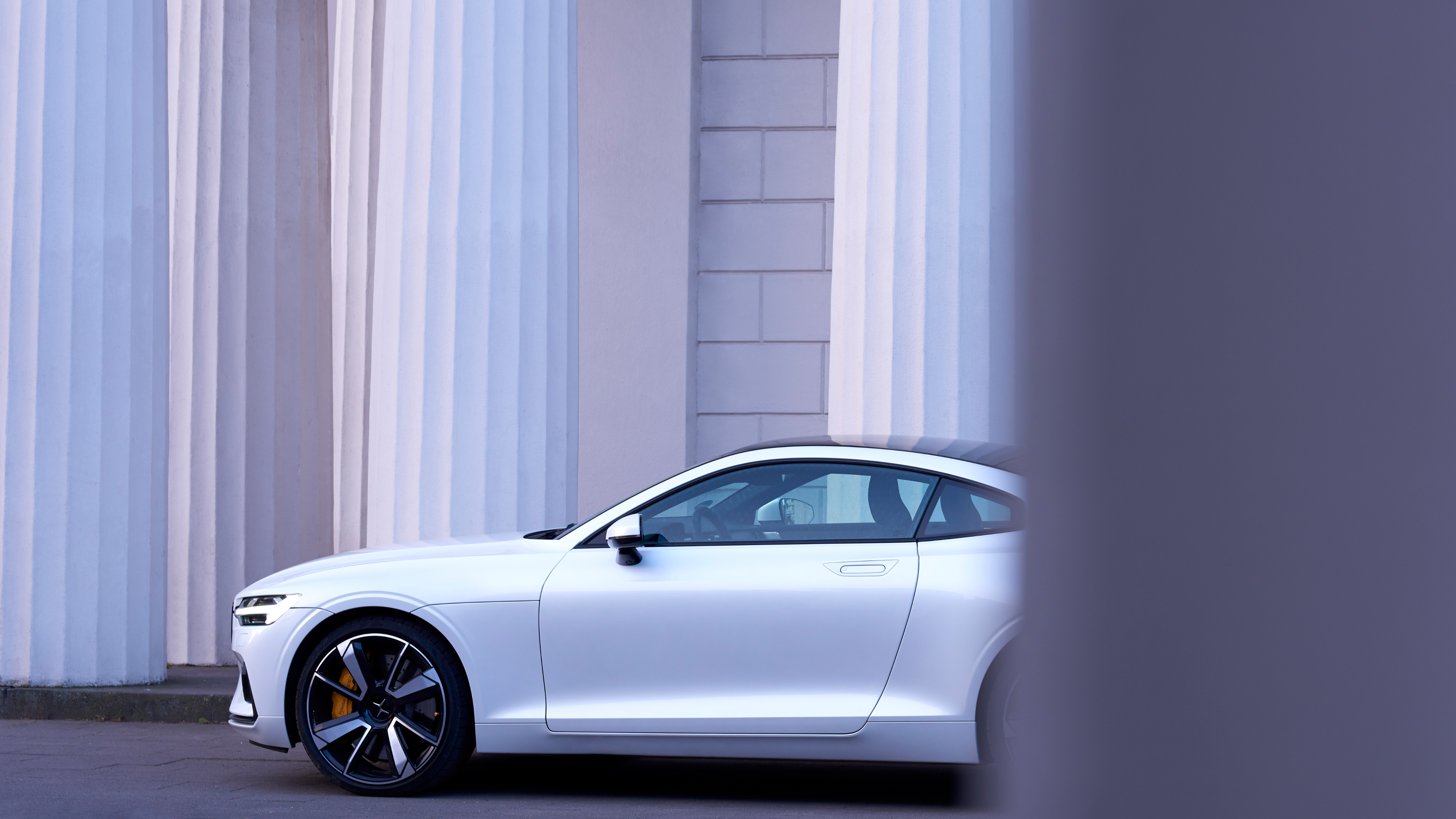 Side view of a white Polestar in front of a white brick wall.