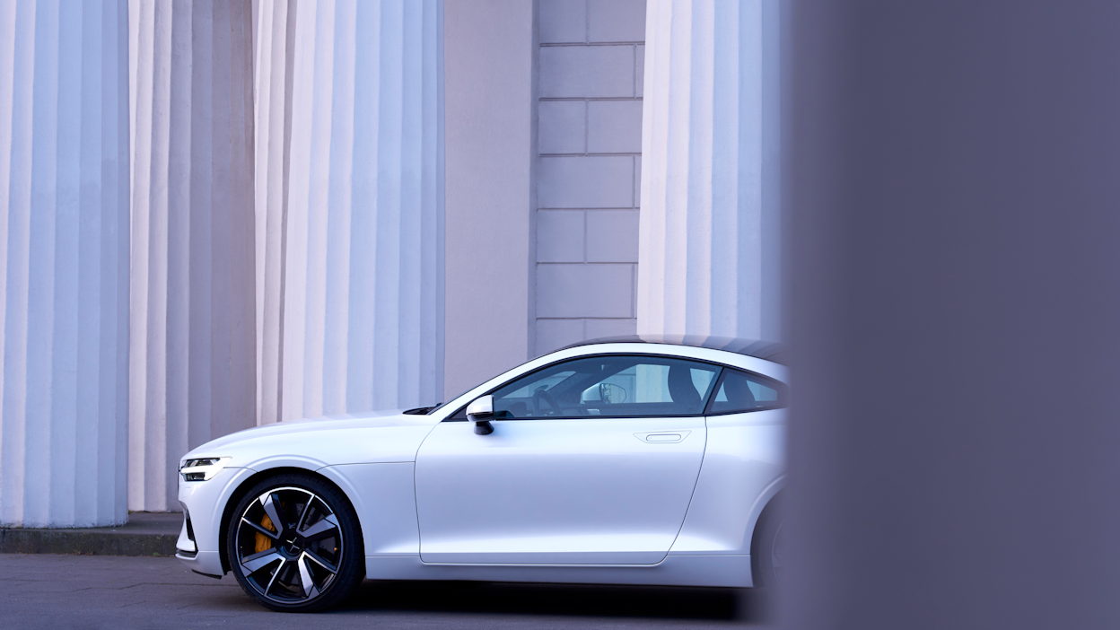 Side view of a white Polestar in front of a white brick wall.
