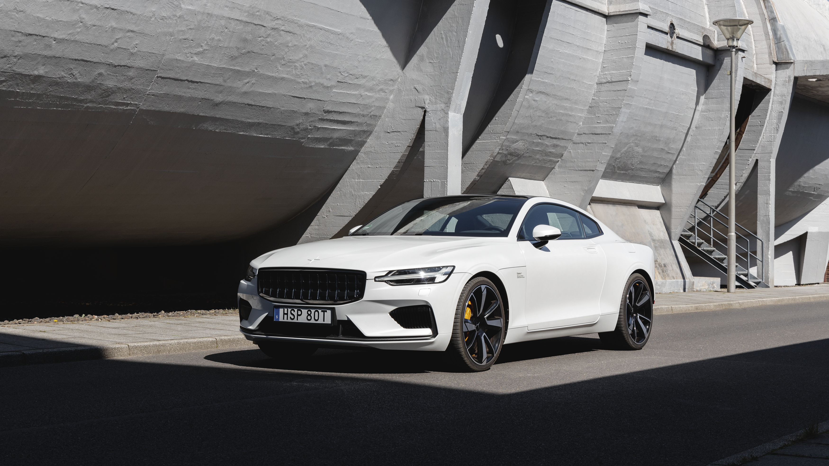 A white Polestar 1 in front of a curved concrete building.