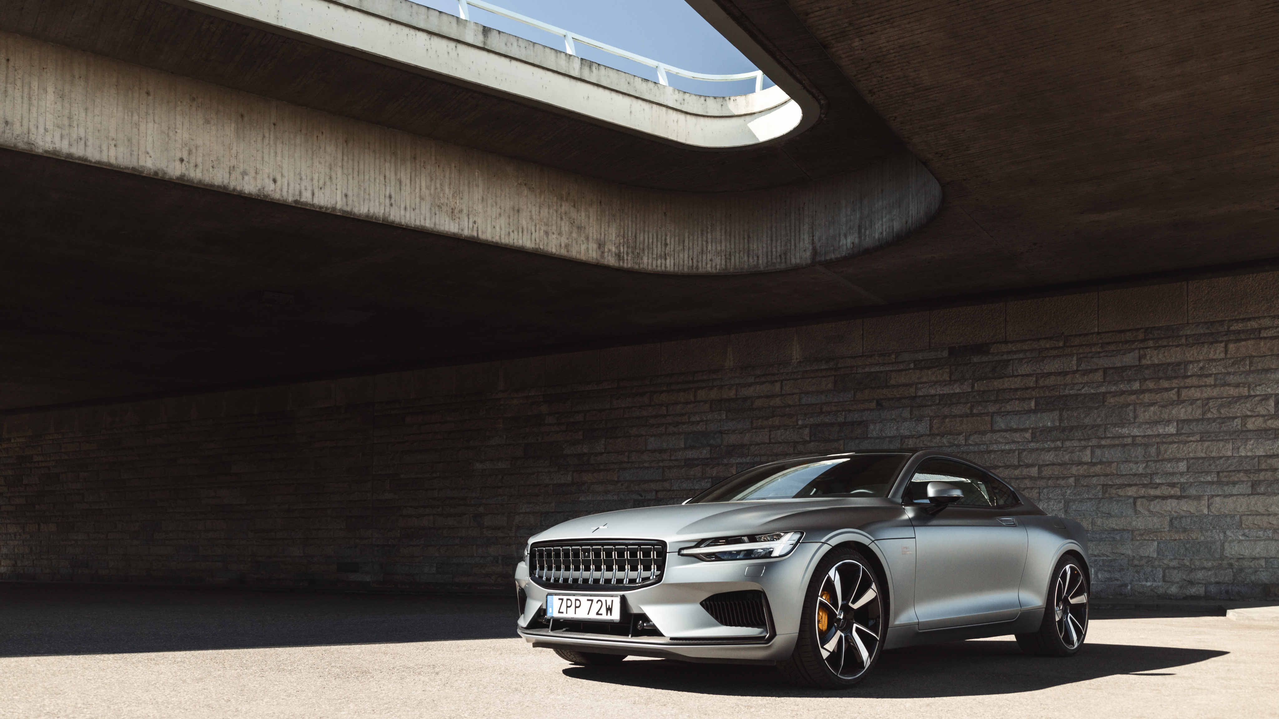 A silver Polestar 1 parked under a bridge.