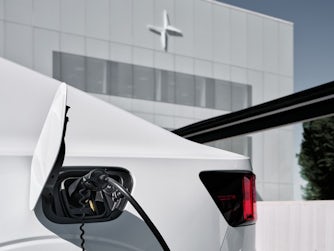 A white Polestar 2 charging outside of a white building.