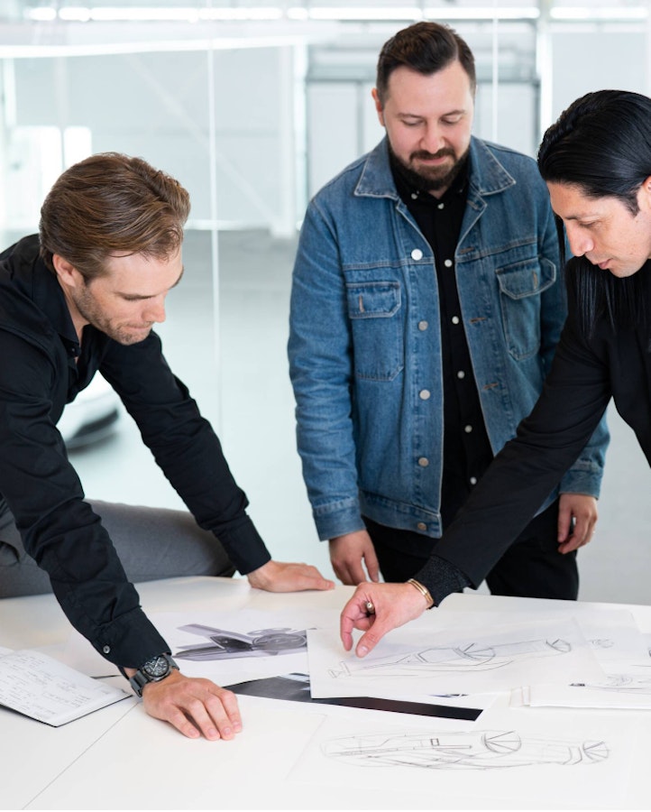 Three people standing at a table looking at design sketches