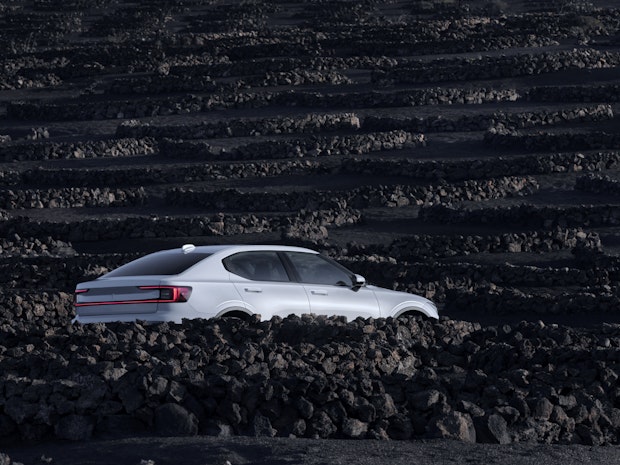 Polestar car parked in a rocky landscape with rows of dark, uneven terrain in the background.