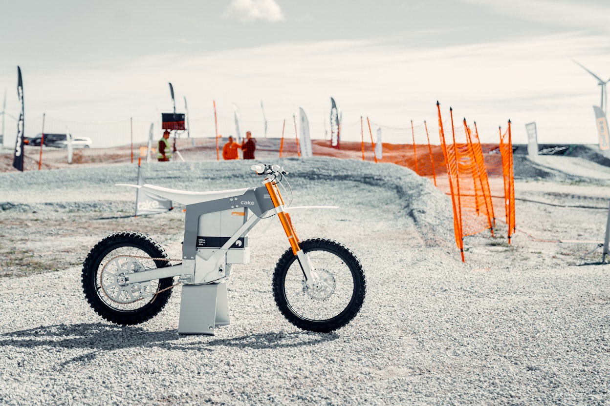 Cake mountain bike displayed on gravel with an orange safety net in the background.