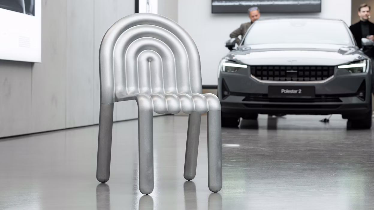 Image of an aluminium chair in front of a Polestar 2.