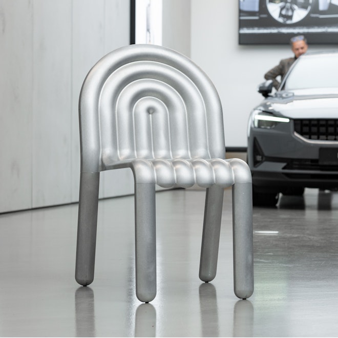 Image of an aluminium chair in front of a Polestar 2. 