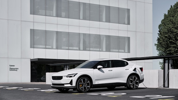 Image of a white Polestar 2 charging in front of white building. 