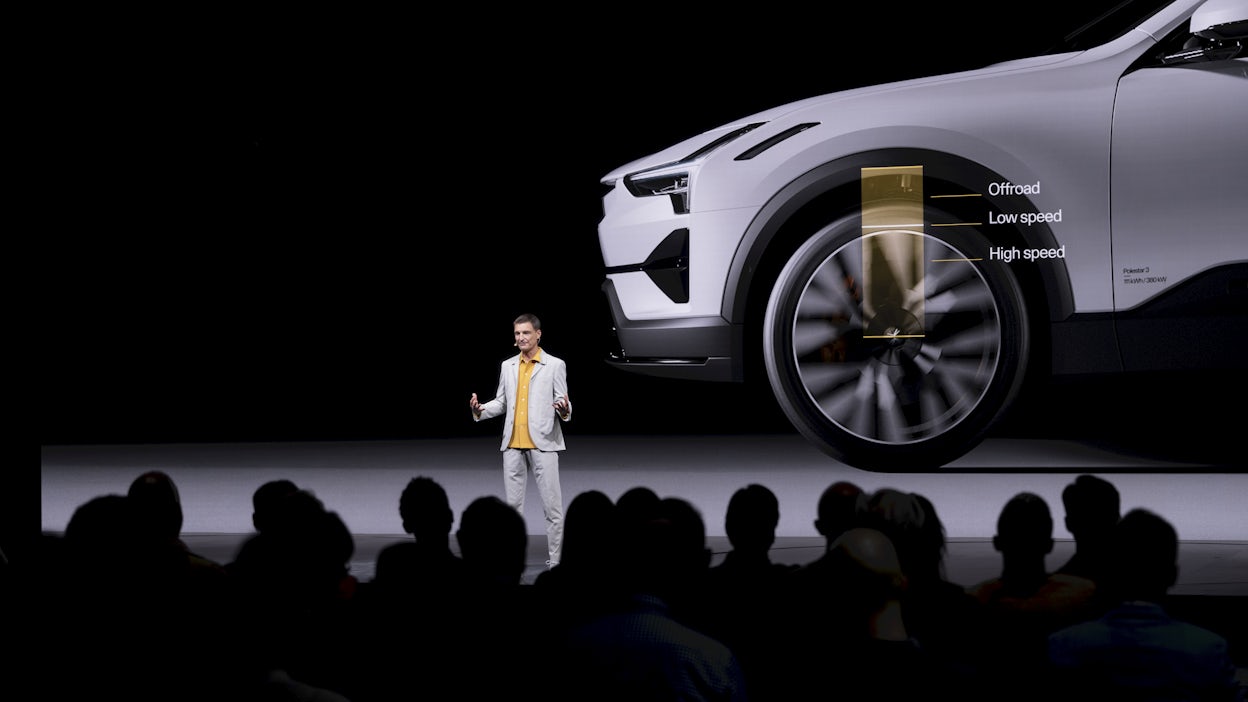 A man standing on stage in front of a screen showing a white car.