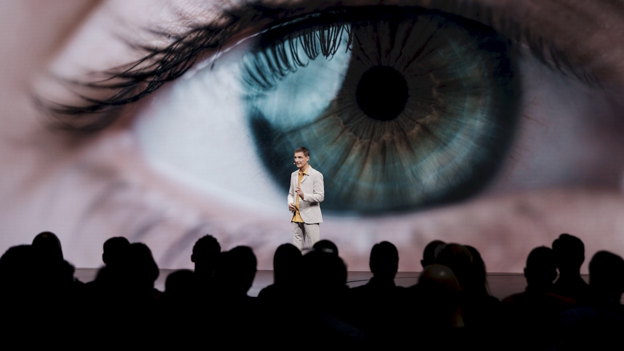 A man standing on stage in front of a screen showing a human eye.