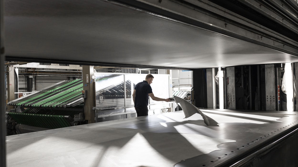 A man placing a large piece of leather onto a table at a workshop.