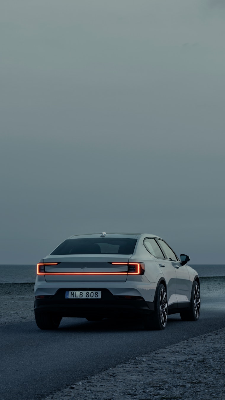 Showing Polestar 2 driving forward on a road along the water.