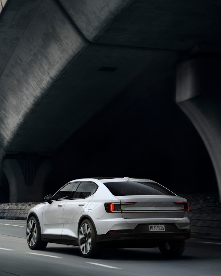 A white Polestar 2 driving on a dark road. Seen obliquely from behind.