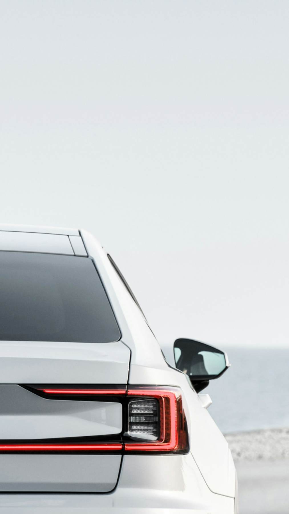 Back view of a parked white Polestar 2 on a road next to the sea