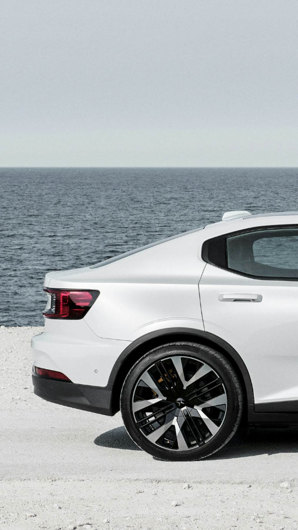 Side view of a white Polestar 2 on a road next to the sea