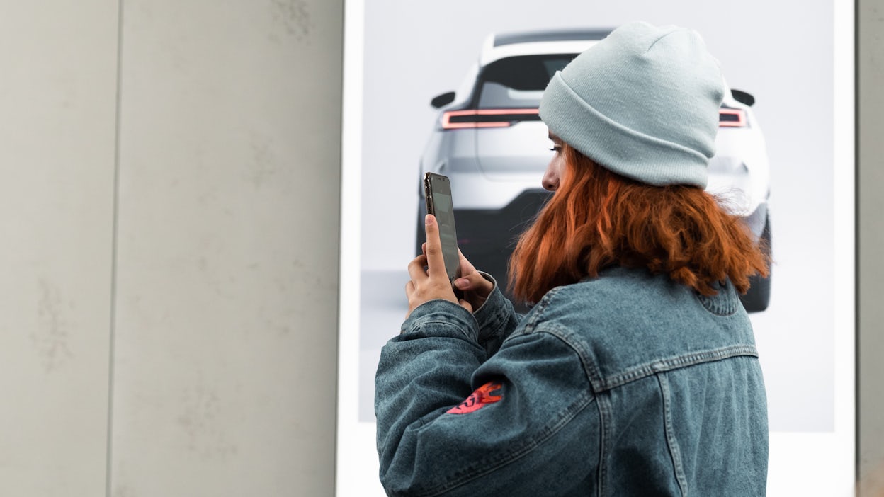 Girl with red hair, jeans jacket and blue cap photographing something in a Polestar space
