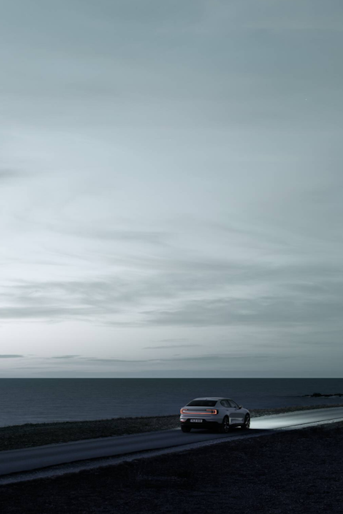 A white Polestar 2 driving on a road next to the ocean.