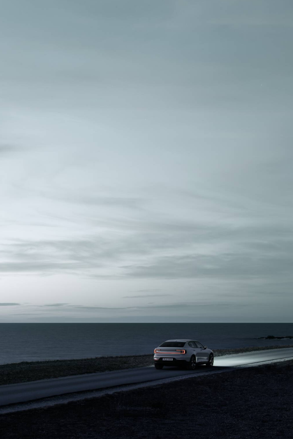 A white Polestar 2 driving on a road next to the ocean.