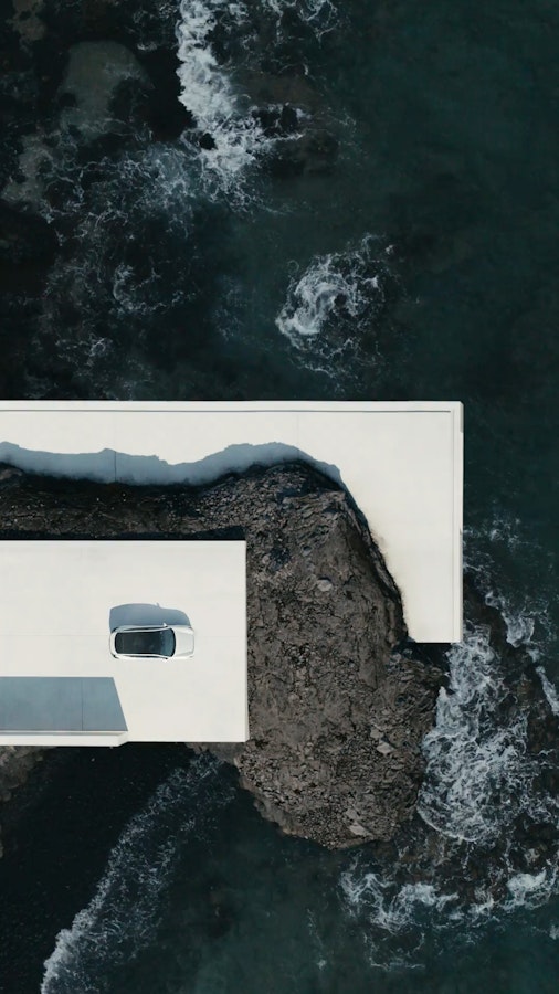 Polestar 3 in white parked on a concrete deck by the coastline with the ocean lapping beneath