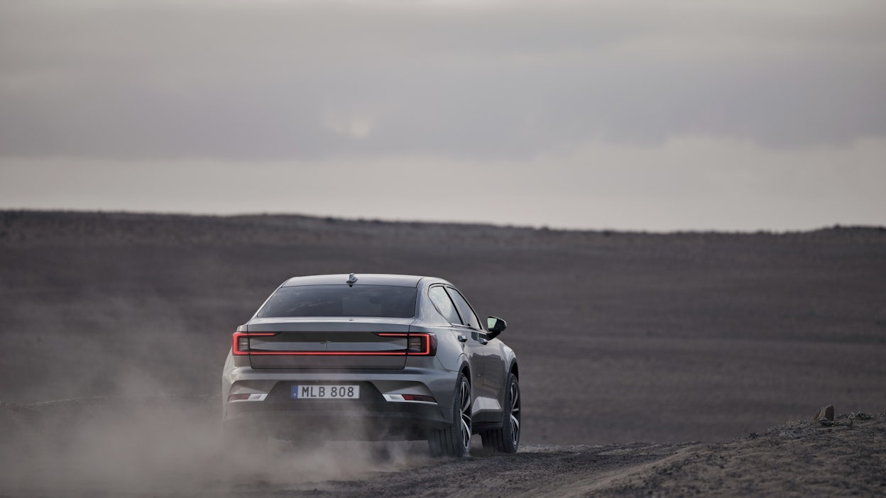 A Polestar 2 driving in a dark desert, light grey sky