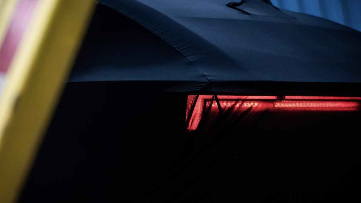 Rear red light of a Polestar car partially covered by fabric in a dimly lit environment.