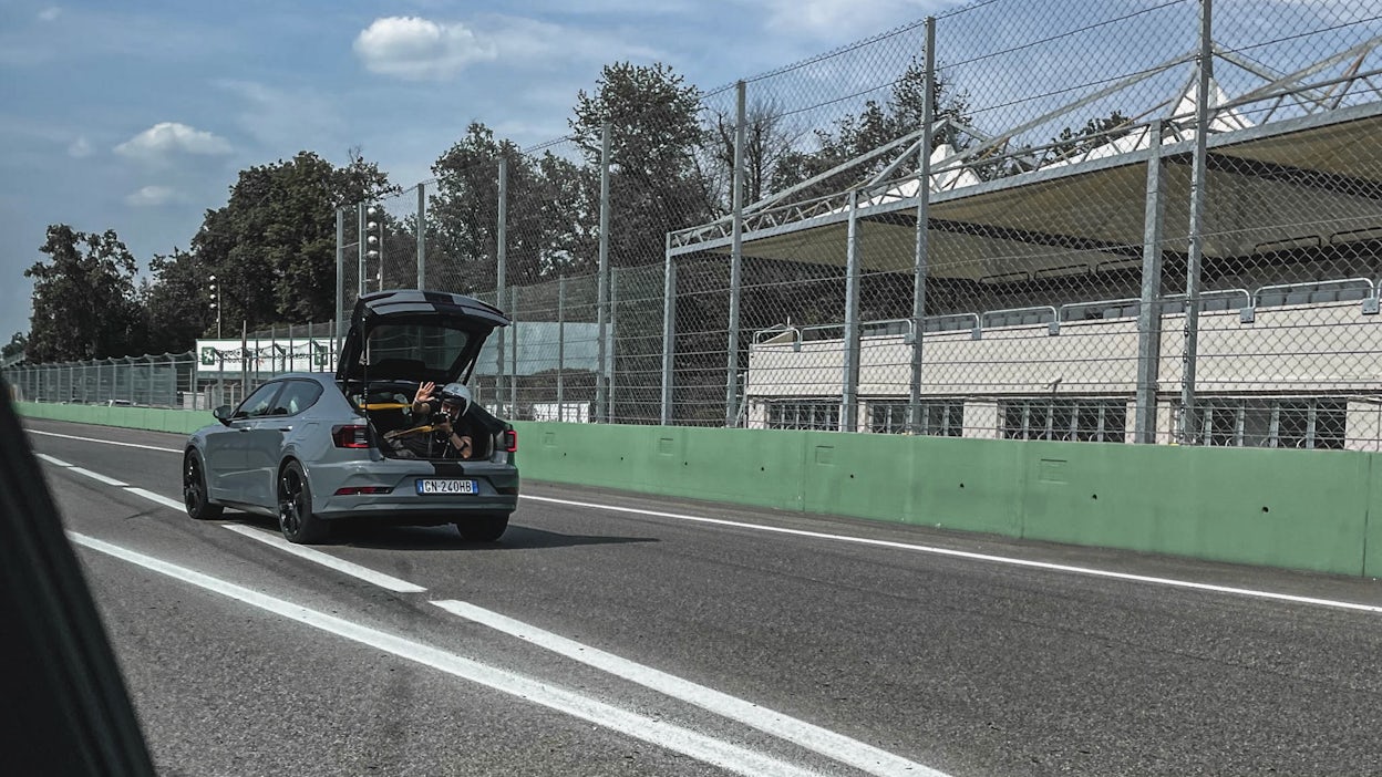 Cameraman waving his hand from the trunk of a Polestar 2 driving on a race track.