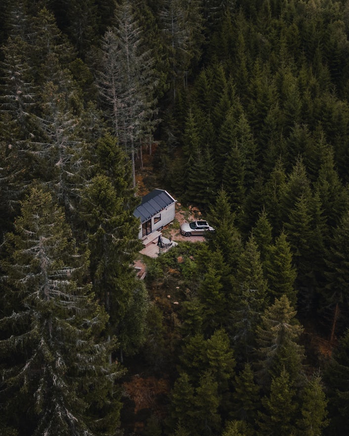 Cabin with Polestar 2 parked in front, surrounded by forest.