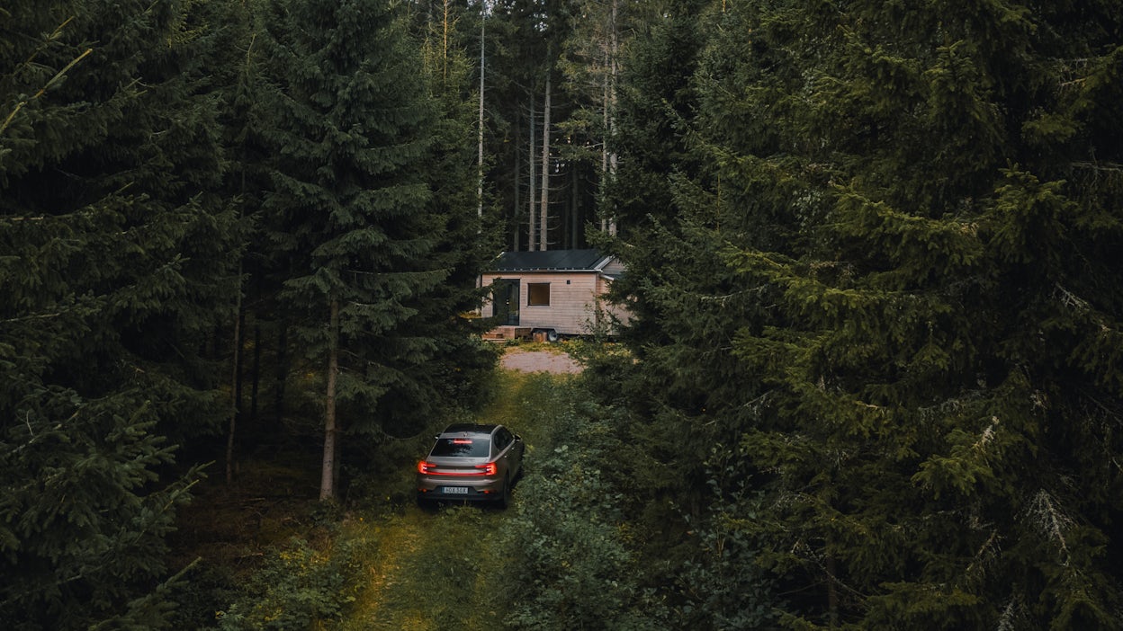 Polestar 2 in front of forest cabin.