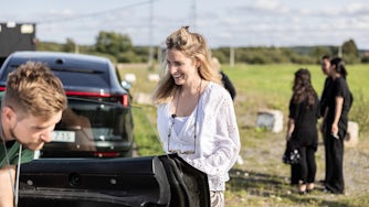 Smiling woman standing next to a car that is parked on the roadside.