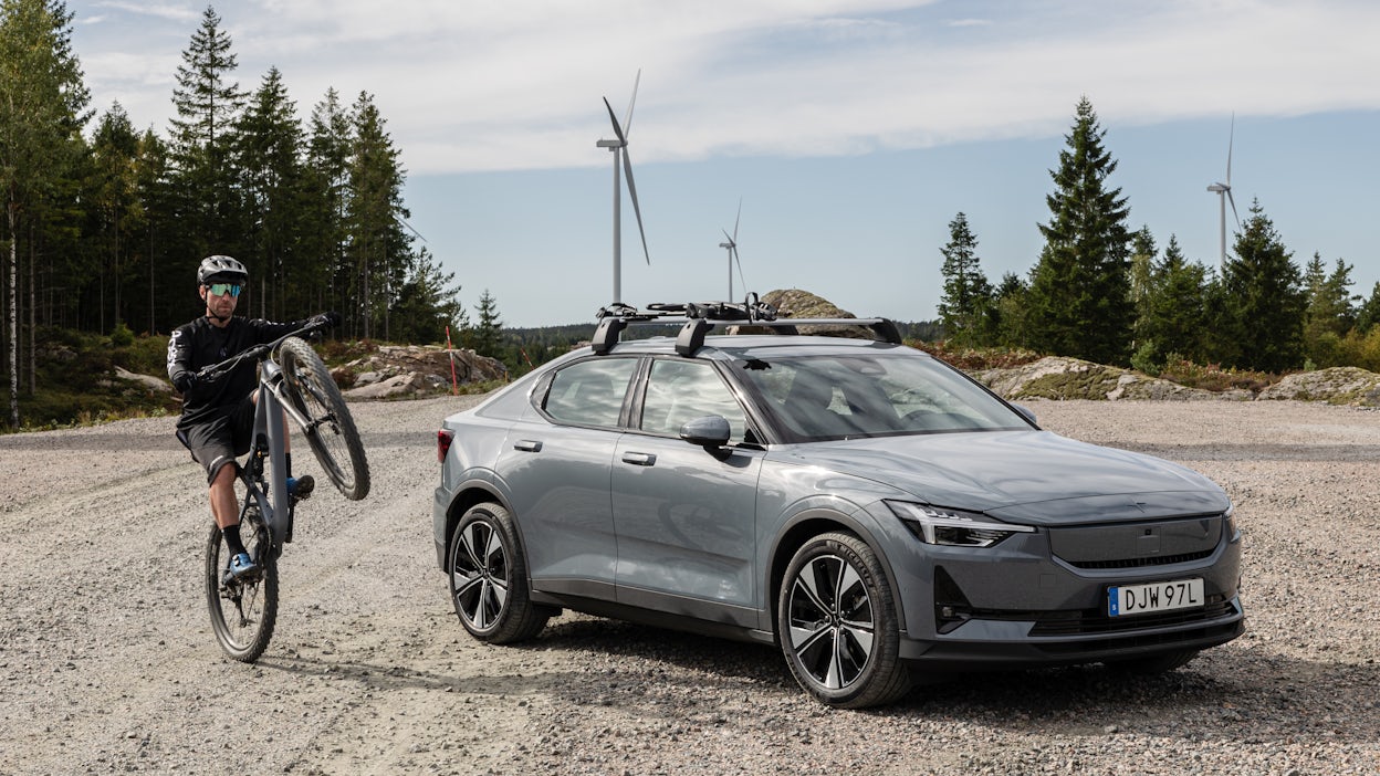 Man doing a wheelie on bike in front of Polestar 2