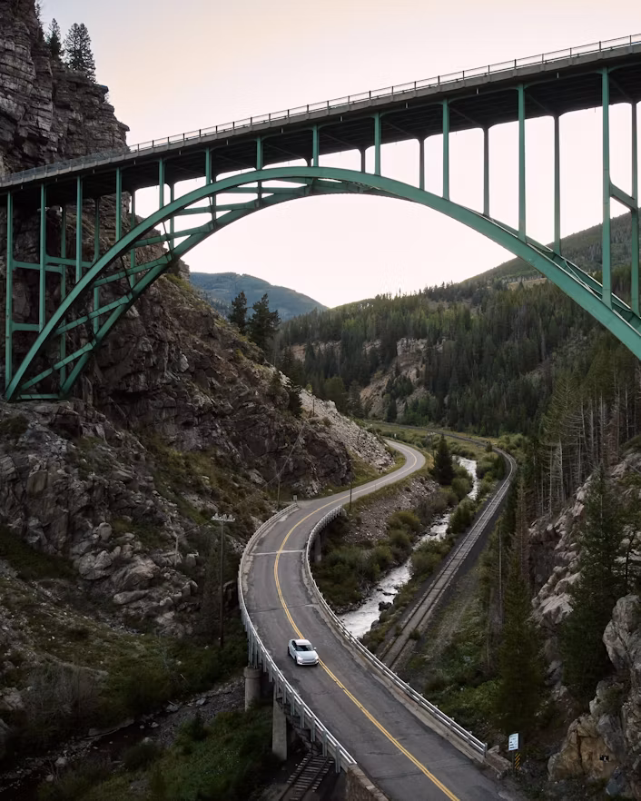 Polestar car on a curved road under a green bridge surrounded by rocky terrain and trees.