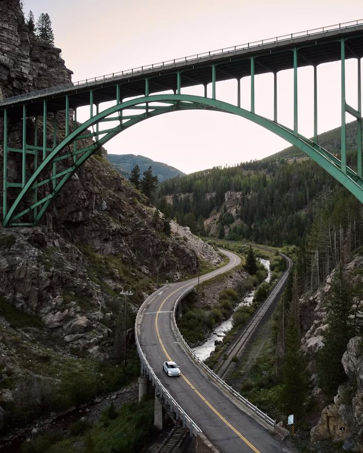 Polestar car on a curved road under a green bridge surrounded by rocky terrain and trees.